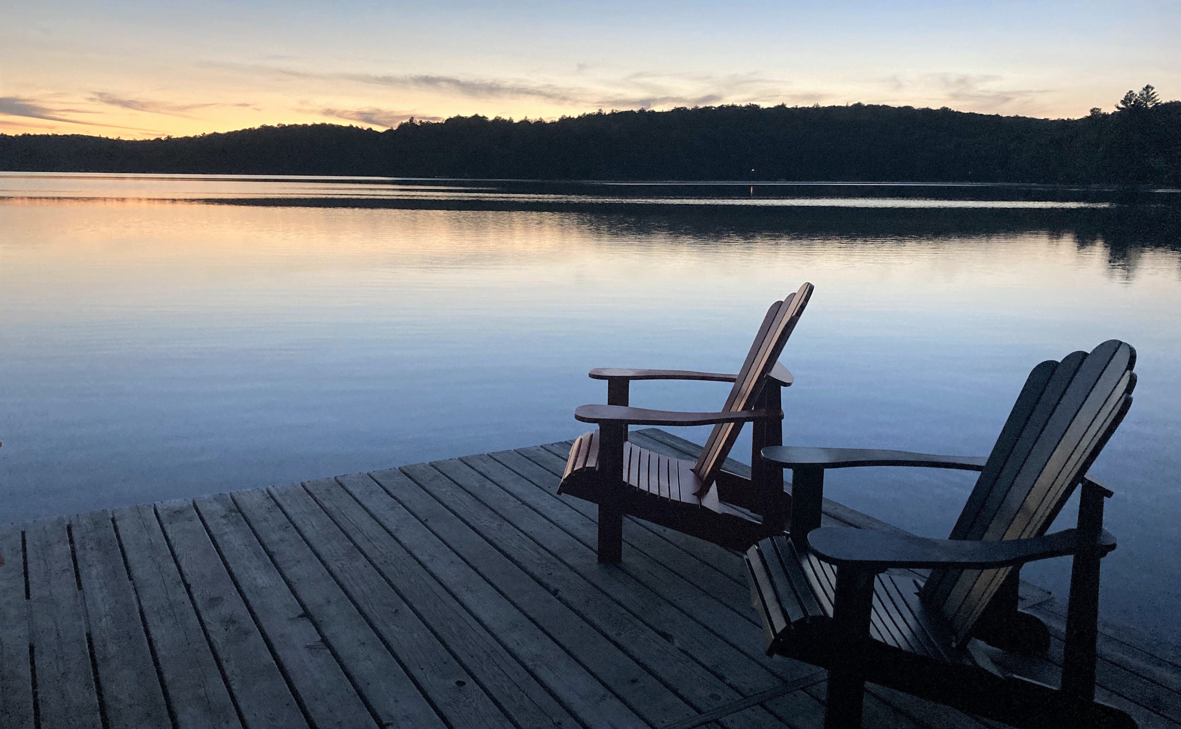Adirondack chairs on dock by the lake at sunset