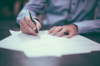 person in a dress shirt writing at a desk