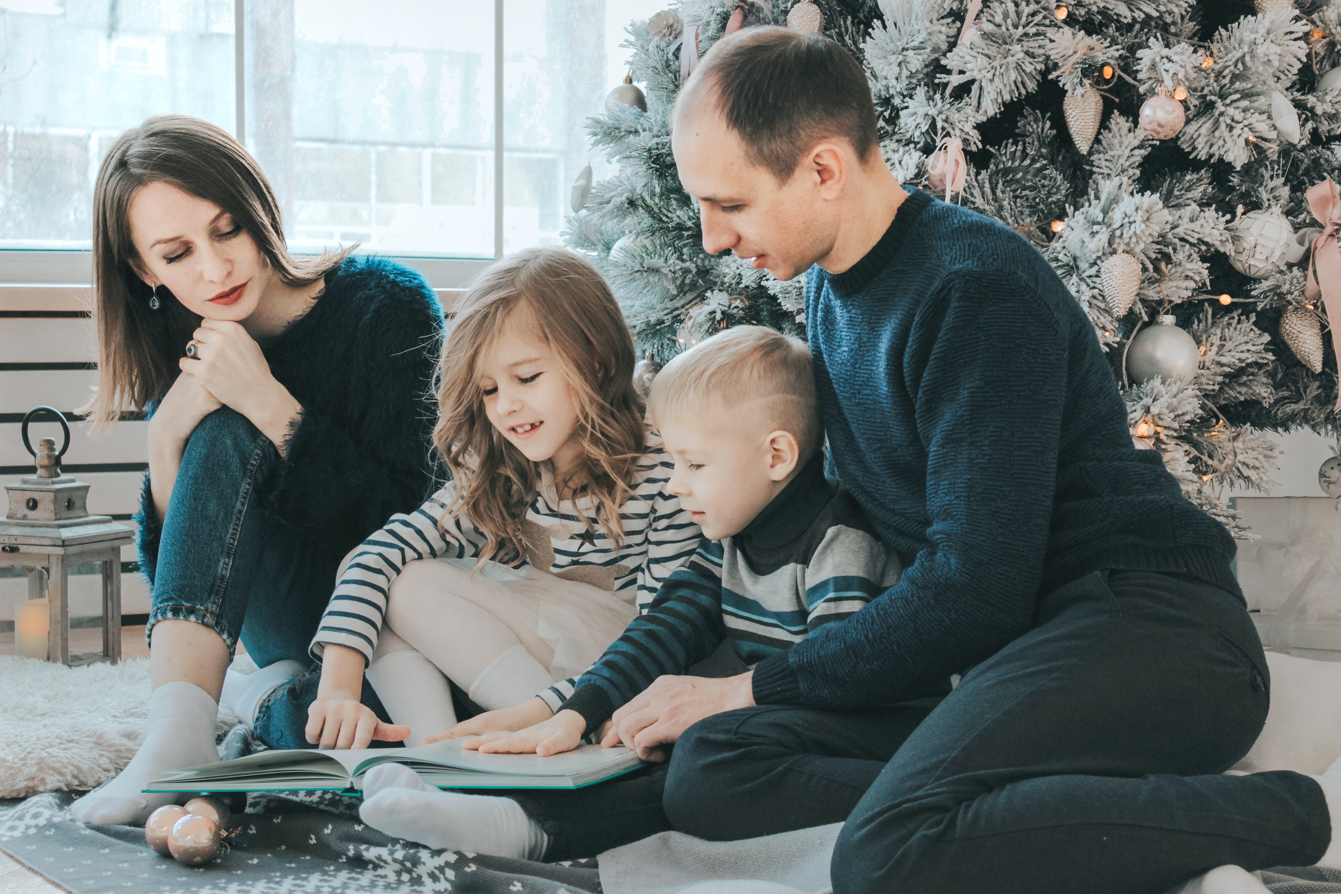 family reading a book in front of Christmas tree