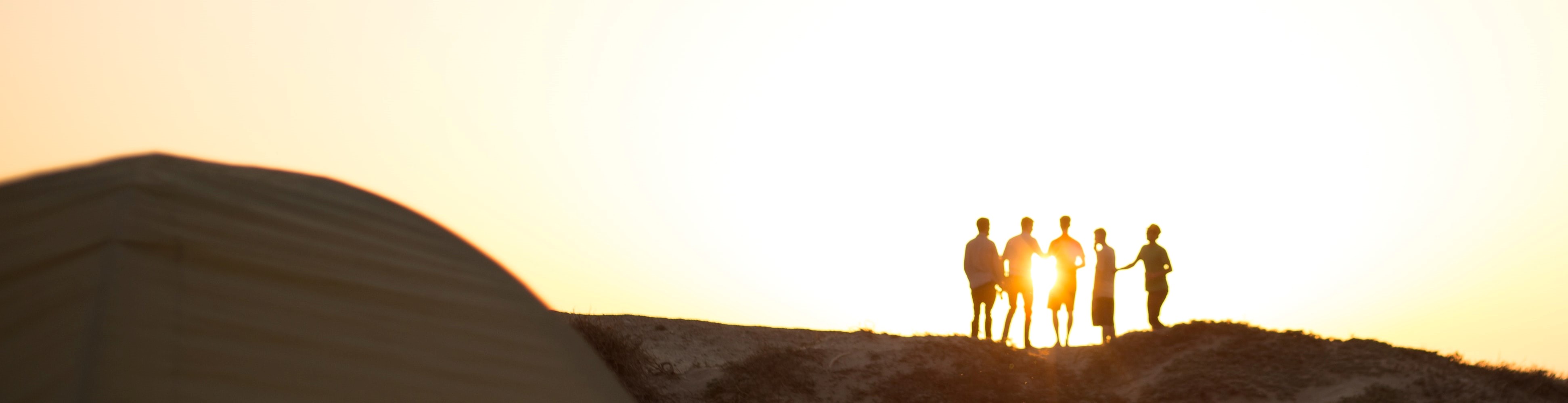 silhouette of friends standing on a hill during sunset 